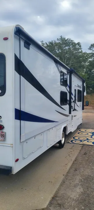 White Sunseeker RV rental, a clean motorhome with black and blue stripe graphics, parked on asphalt under a cloudy sky.. Forest River Sunseeker LE 2020