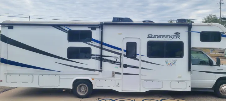 This white Sunseeker Class C RV rental, with blue and black graphics, is equipped for travel adventures.. Forest River Sunseeker LE 2020