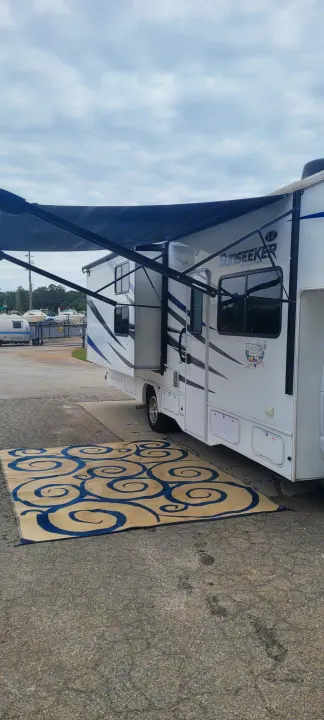 A white RV rental with its awning extended over a large blue and cream patterned outdoor rug.. Forest River Sunseeker LE 2020
