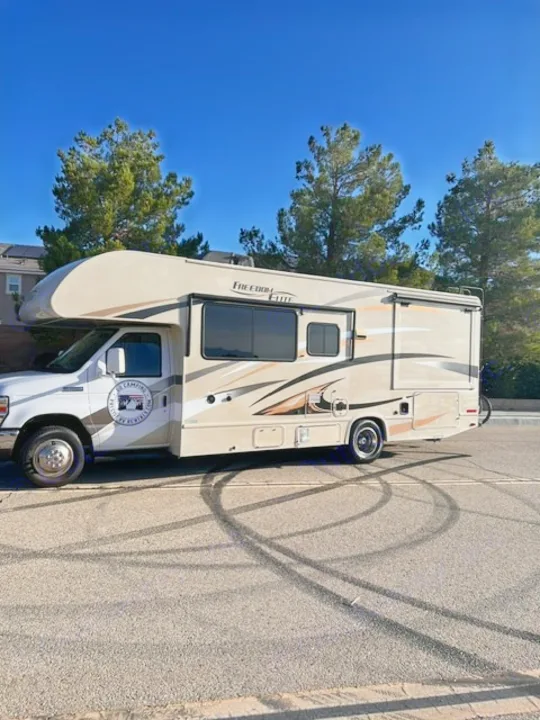 Tan Class C motorhome RV rental parked on asphalt with tire marks under a clear sky.. Thor Motor Coach Freedom Elite 2017