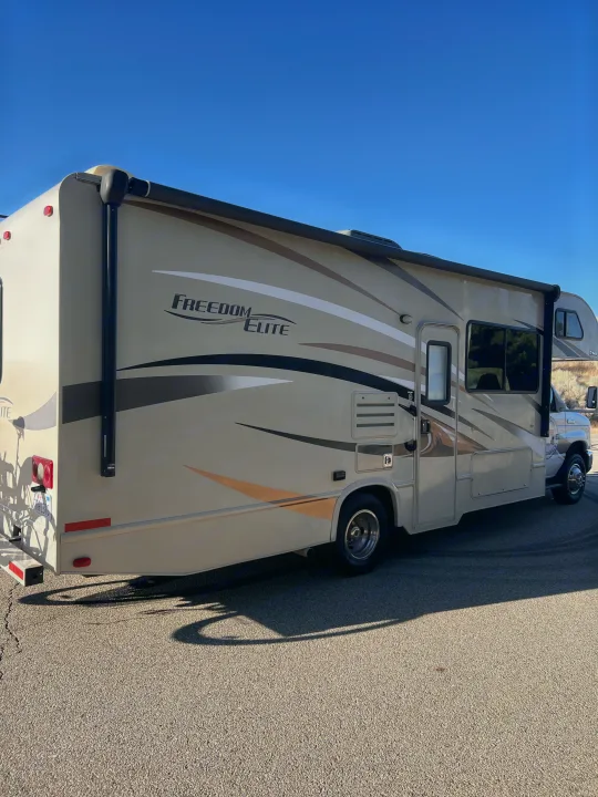 Discover adventure with this Freedom Elite RV rental, featuring scenic graphics, parked under a sunny blue sky.. Thor Motor Coach Freedom Elite 2017