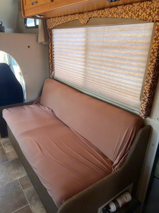 Inside a comfortable RV rental: a plush peach sofa bed, wide window with blinds, and wood cabinetry create a welcoming camper living space.. Thor Motor Coach Freedom Elite 2017