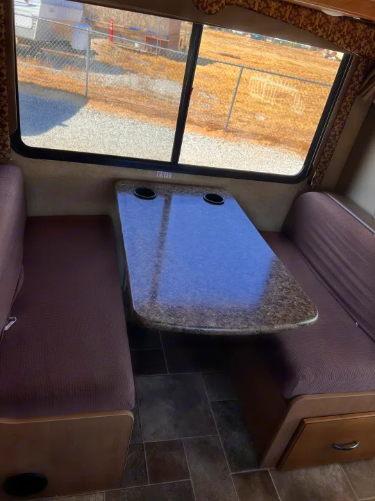 RV rental dinette features textured brown benches, a speckled table with cup holders, and bright windows with outdoor views.. Thor Motor Coach Freedom Elite 2017