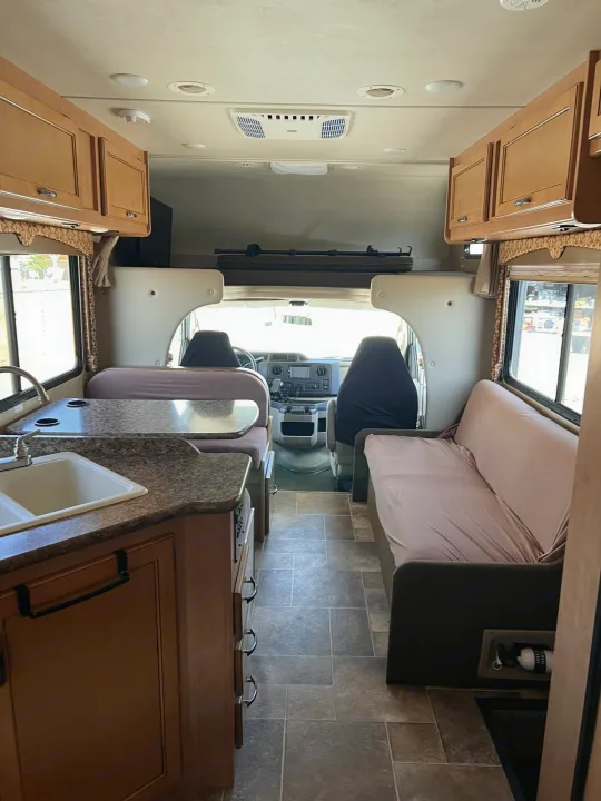 Explore this rv rental's inviting interior: kitchen sink, dining booth, lounge sofa, and cockpit. Ideal for road trips.. Thor Motor Coach Freedom Elite 2017