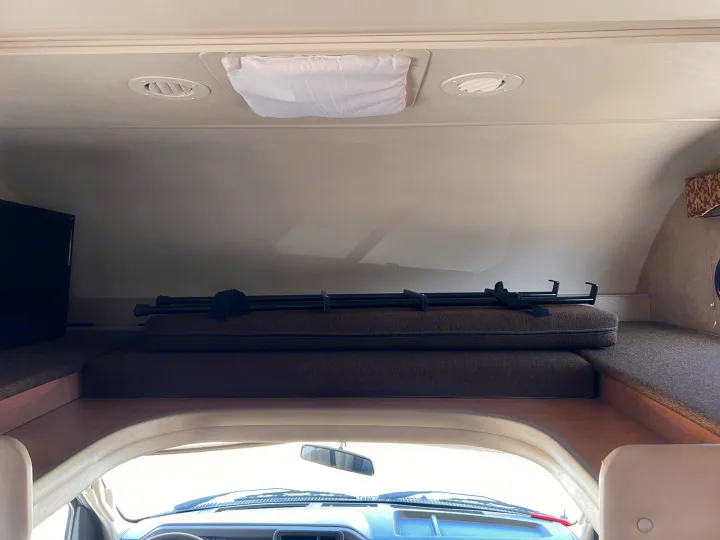 RV rental interior: over-cab bunk with mattress & support bars. Ceiling vents, a covered vent, & TV. View from the driver's seat.. Thor Motor Coach Freedom Elite 2017