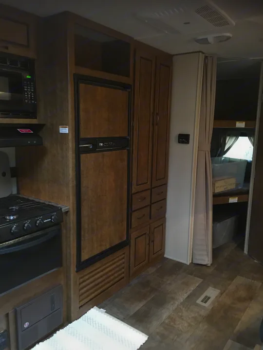 RV rental interior: A functional kitchen with microwave and stove, built-in fridge, extensive storage, and a private bunk area.. Crossroads RV Zinger 2016