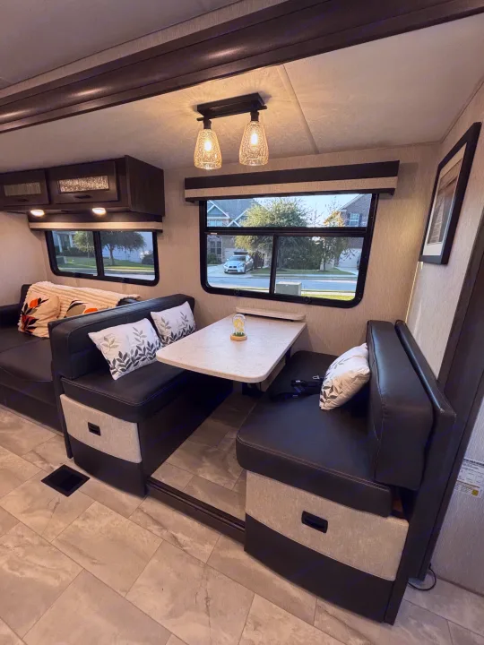 Spacious RV rental living area featuring a comfortable dinette with black leatherette seating, a cozy sofa, and large windows.. Winnebago Coachmen 35ES Class A RV 2024