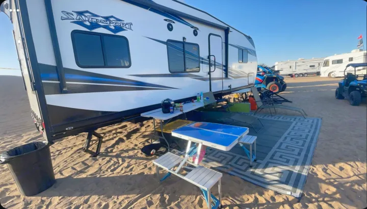 White Sand Sport RV rental parked on sand, with an outdoor setup, and other off-road vehicles & RVs in the desert.. Pacific Coachworks Sandsport 2022