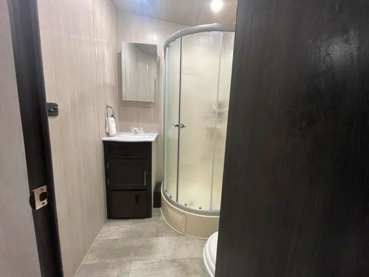 Inside an RV rental, this clean, compact bathroom offers a vanity with sink, mirror, and a curved shower enclosure.. Pacific Coachworks Sandsport 2022