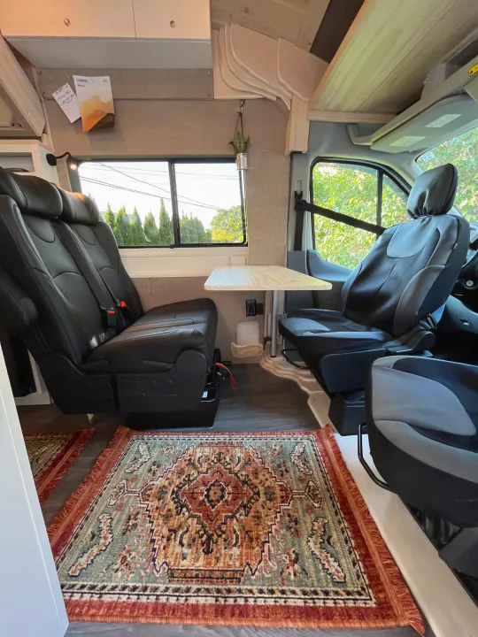 Cozy RV rental interior: comfortable seating, wooden table, & colorful rug, perfect for road trip adventures.. Custom Built Transit 2017