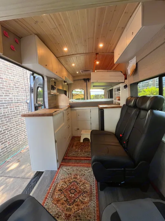 RV rental: Inside a modern converted camper van with a wood ceiling, kitchen, bed, and comfortable passenger seating.. Custom Built Transit 2017