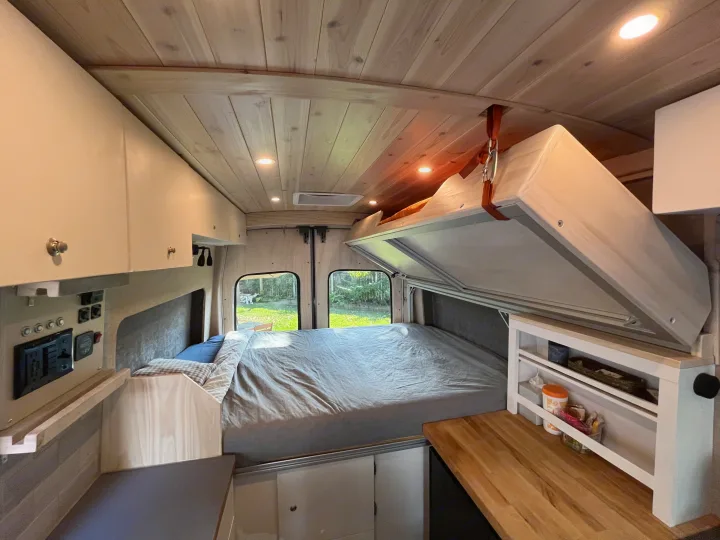 RV rental: Cozy camper van interior with lift bed, wooden ceiling, and kitchen counter for comfortable travel.. Custom Built Transit 2017