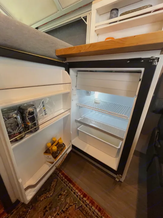 RV rental's compact fridge is open, showcasing beverages and a freezer, a convenient amenity for your adventures.. Custom Built Transit 2017