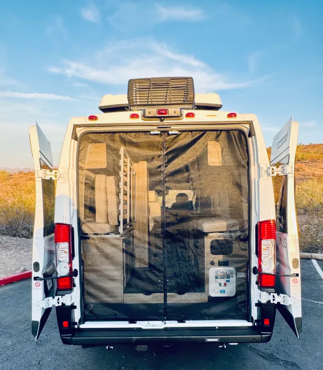 Rear of an RV rental camper van with open doors, showing a full-size mesh screen, organized interior, & desert scenery.. Winnebago Solis 59PX 2025