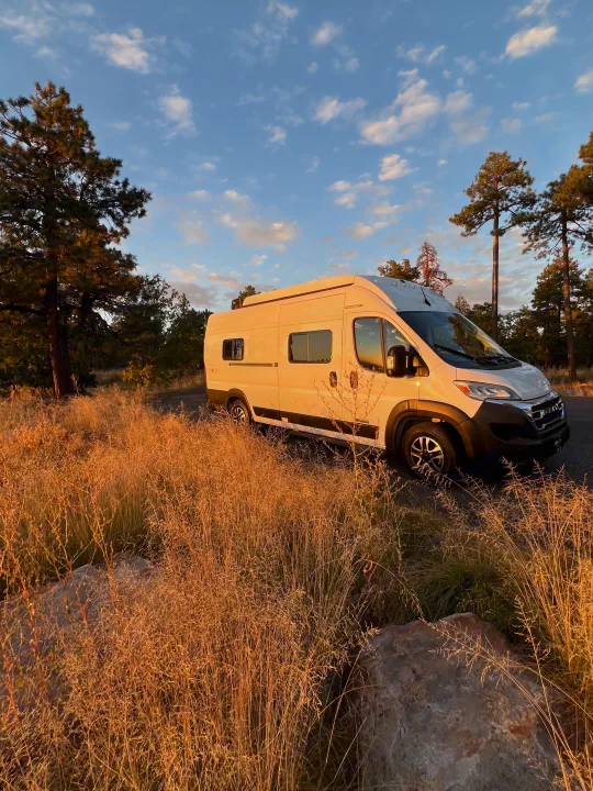 White camper van RV rental gleaming in golden hour sun amidst tall grasses and trees. Your nature adventure awaits!. Winnebago Solis 59PX 2025
