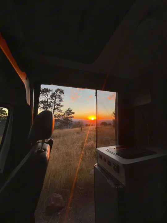 Stunning sunset from our RV rental. Golden light illuminates a vast, grassy landscape outside our van. Perfect end to a day outdoors.. Winnebago Solis 59PX 2025