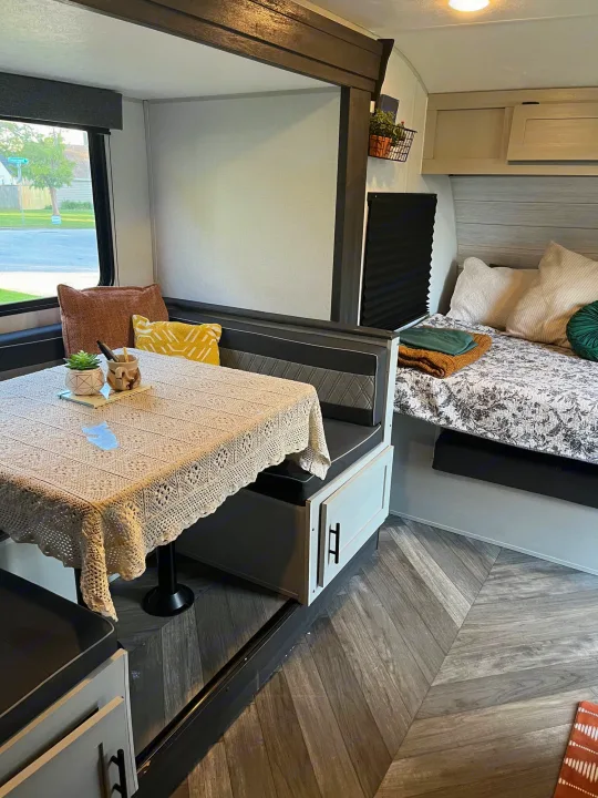 Cozy RV rental interior: a dinette with a crochet tablecloth, and a bed with a patterned quilt and pillows.. Forest River Wildwood FSX 2021
