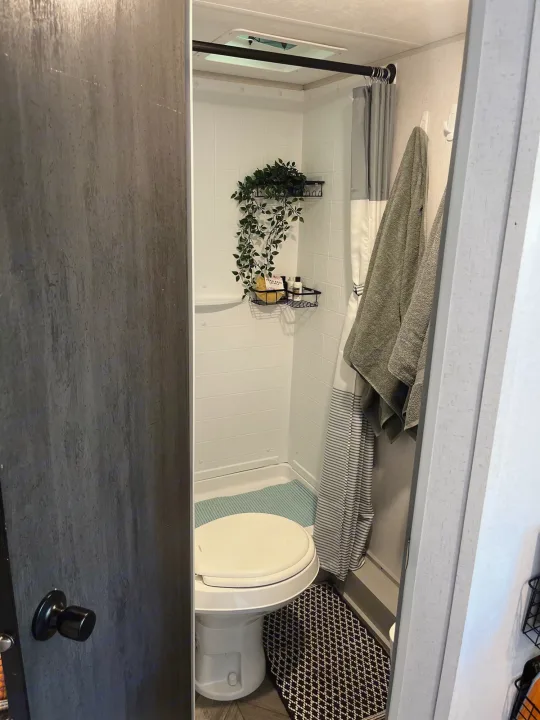 Inside a modern RV rental bathroom: compact shower, white toilet, and hanging towels. Essential amenities for travel.. Forest River Wildwood FSX 2021