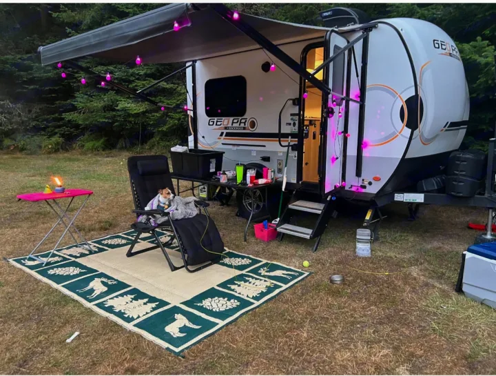 Cozy RV rental camping setup with a dog, awning, and festive lights at dusk.. Forest River Rockwood Geo Pro 2023