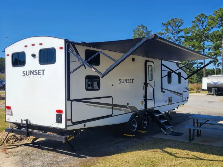 A white Sunset Trail RV with an extended awning is parked in a sunny outdoor setting, ideal for an rv rental adventure.. Crossroads Sunset Trail Super Lite 2022