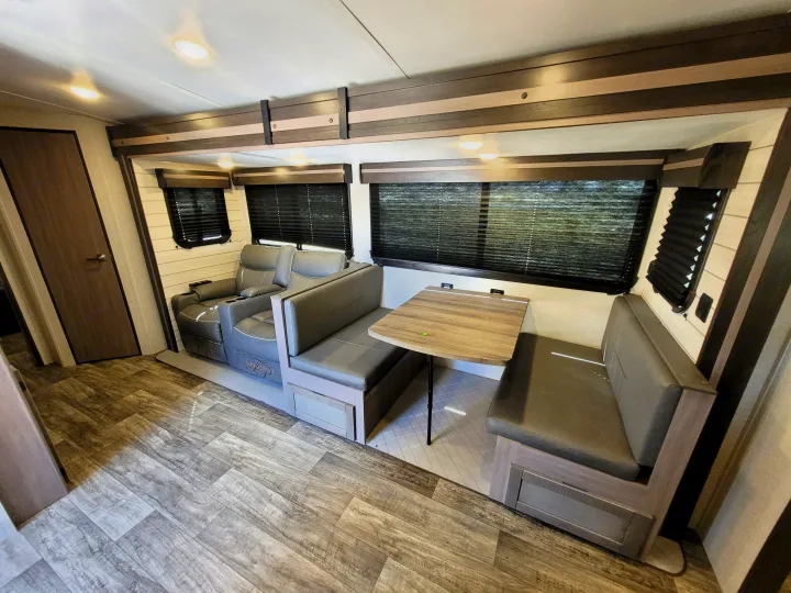 Inside a modern RV rental: grey recliners, a cozy booth dinette with table, and wood-look flooring. Ready for adventure.. Crossroads Sunset Trail Super Lite 2022