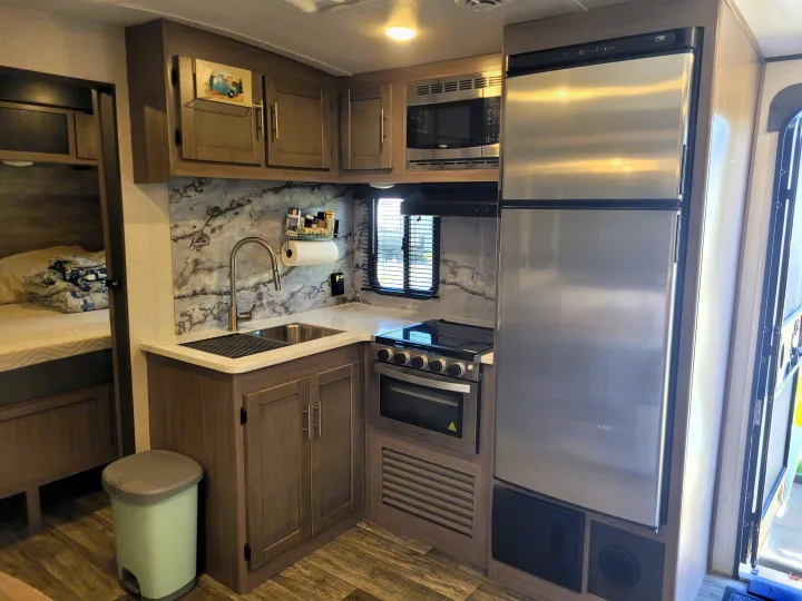 Well-equipped RV rental kitchen & living space with full appliances: sink, stove, microwave, fridge, plus a cozy bed.. Crossroads Sunset Trail Super Lite 2022