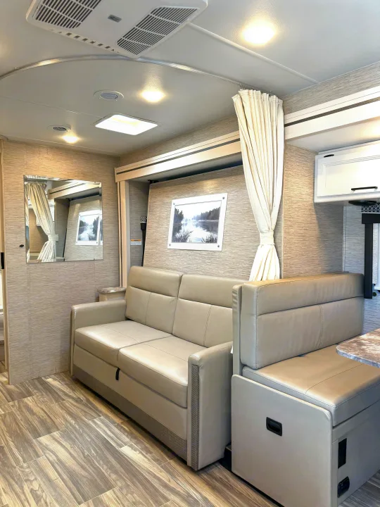 Bright RV rental living space: modern light-toned sofa/sleeper, dinette, and wood-look flooring for travel comfort.. Thor Vegas 2023