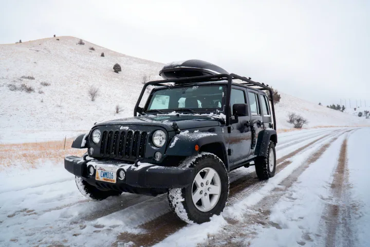 Dark green Jeep Wrangler with roof cargo box on a snowy winter road. Perfect for off-road adventure or an RV rental trip.. Jeep Wrangler Unlimited 2018