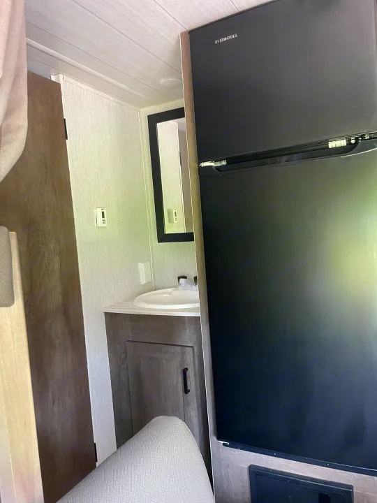 RV rental interior featuring a black Everchill refrigerator, compact bathroom vanity with sink, and a digital thermostat.. Forest River Wildwood X-Lite 2022