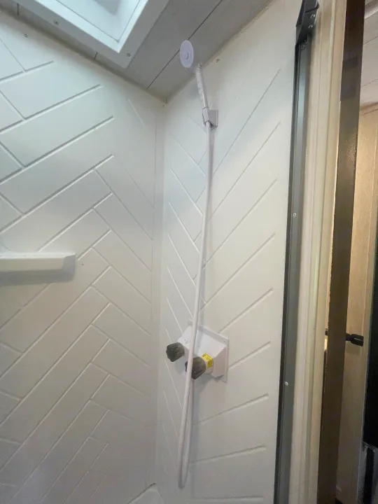 A practical shower inside an RV rental, featuring white herringbone walls, a handheld shower, and faucet controls.. Forest River Wildwood X-Lite 2022
