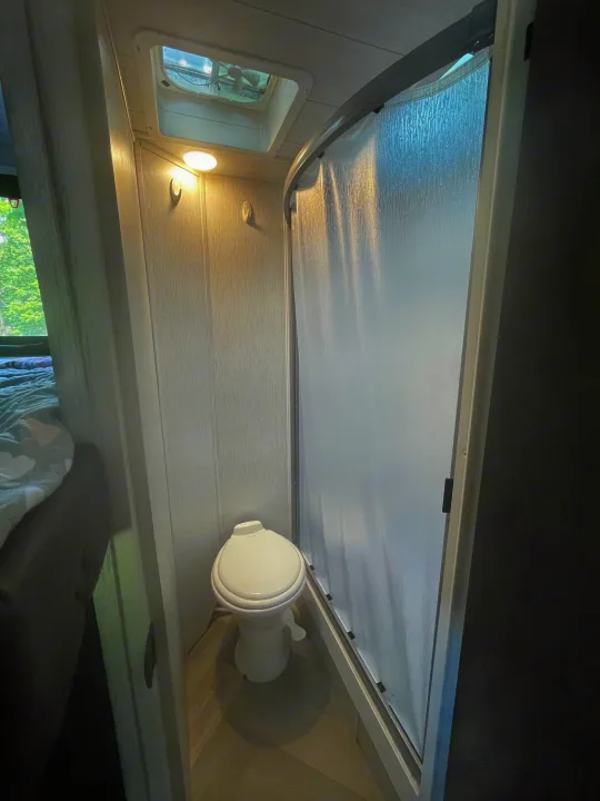 Compact RV rental bathroom with toilet, a textured sliding shower door, and an overhead vent, maximizing space.. Forest River Wildwood X-Lite 2022