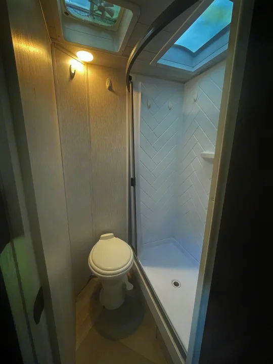 Clean RV rental bathroom with a compact toilet and bright shower featuring a skylight and herringbone tiles.. Forest River Wildwood X-Lite 2022