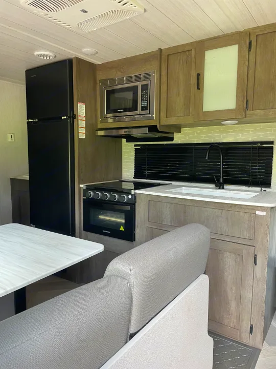 Modern rv rental interior showing a full kitchen with a fridge, stove, microwave, sink, and dining seating.. Forest River Wildwood X-Lite 2022