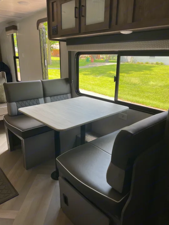 Inside this RV rental: a modern dinette with comfortable booth seating, a table, and large windows showcasing the outdoors.. Forest River Wildwood X-Lite 2022