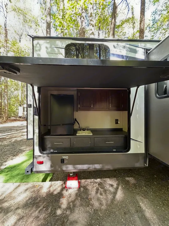 This RV rental features an open outdoor kitchen with fridge, sink, and cabinets, perfect for camping fun in nature.. Palomino Solaire 2018