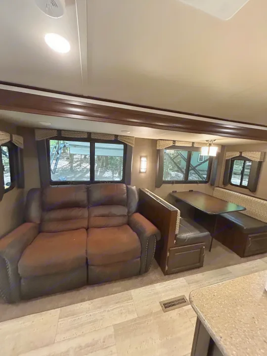 Spacious RV rental interior featuring a comfy sofa, dining booth, and large windows overlooking nature.. Palomino Solaire 2018