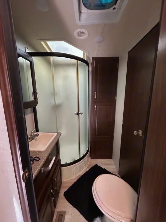 Compact RV rental bathroom with a curved shower, sink vanity, and toilet.. Palomino Solaire 2018