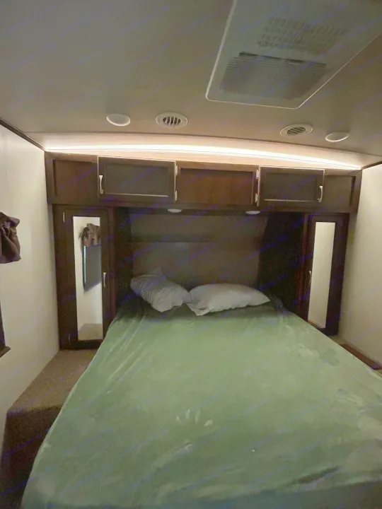 Cozy RV rental bedroom featuring a comfortable bed, wood cabinets, ceiling AC vents, and ambient lighting.. Palomino Solaire 2018