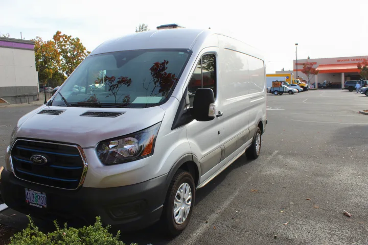 A modern silver Ford E-Transit van, a popular base for RV rental conversions, parked in a bright outdoor lot.. Ford Transit 2023