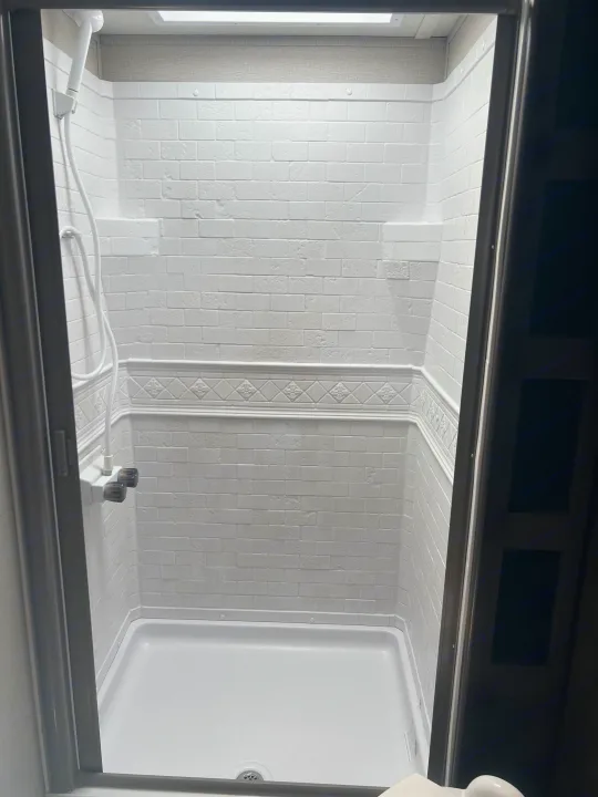 Clean, white RV rental shower stall with brick-patterned walls, a handheld showerhead, and a skylight for comfortable travel.. Grand Design Transcend 2021