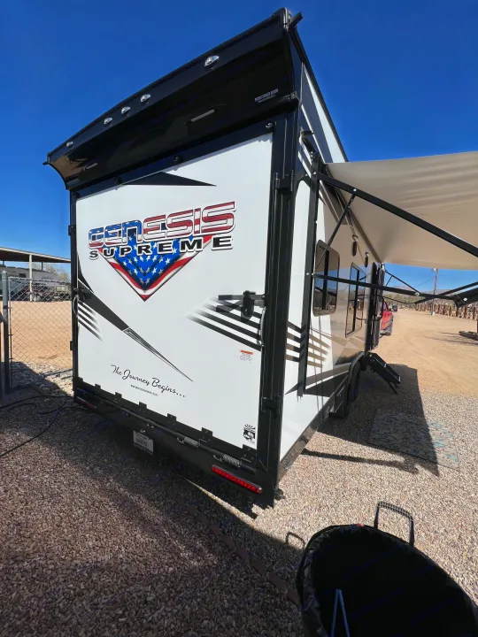 Stylish Genesis Supreme toy hauler RV rental parked on gravel. Awning extended for outdoor living.. Genesis Supreme Rv Genesis Supreme 2022