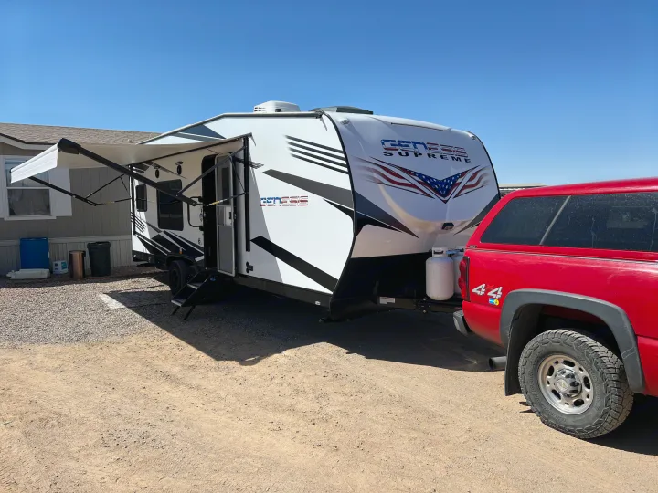 White Genesis Supreme travel trailer RV rental, with awning out, hitched to a red pickup truck on a sunny day.. Genesis Supreme Rv Genesis Supreme 2022
