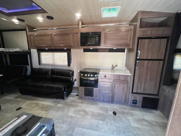 Explore this RV rental's well-equipped interior: kitchen with microwave, fridge, oven, sofa, and ample cabinets.. Genesis Supreme Rv Genesis Supreme 2022