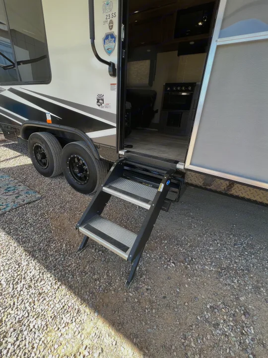RV rental: Three-step entry leads into an open RV door, revealing a kitchen area inside. Parked on gravel.. Genesis Supreme Rv Genesis Supreme 2022