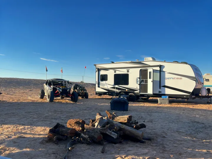 An RV rental, a white travel trailer, set up for desert camping with off-road vehicles and firewood for a fire pit.. Genesis Supreme Rv Genesis Supreme 2022
