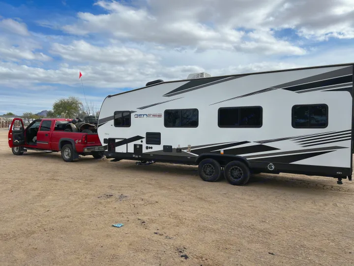 Red pickup truck towing a Genesis toy hauler RV rental in the desert, with ATVs in the truck bed. Ready for adventure!. Genesis Supreme Rv Genesis Supreme 2022