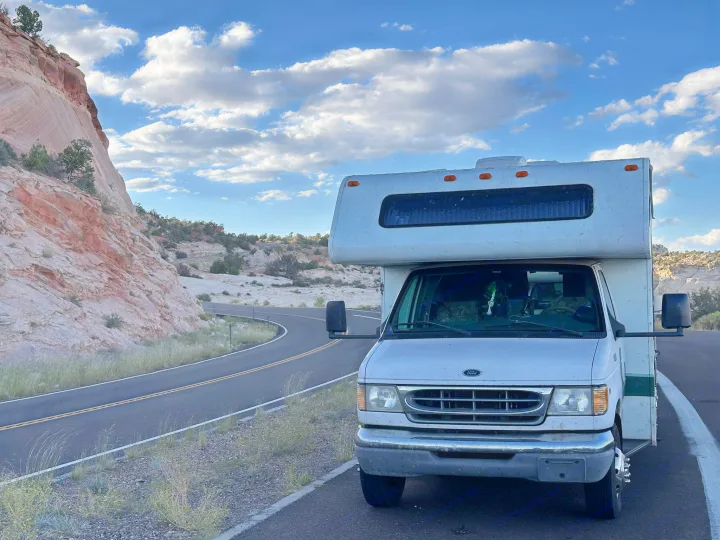 Class C RV rental parked roadside next to red rock cliffs and a winding road under a cloudy blue sky.. Four Winds 5000 2008