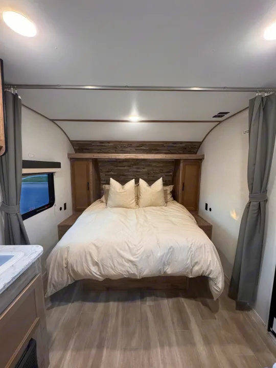 Modern RV rental bedroom with a comfortable bed, stylish wood headboard, and window view. Ideal for adventures.. Grand River 25BH 2025