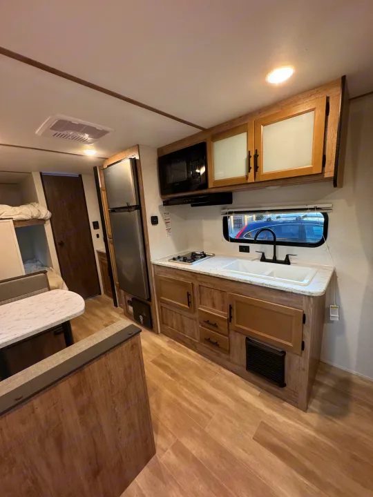 RV rental interior featuring a modern kitchen with a sink, stove, microwave, fridge, plus a dining area & bunk beds.. Grand River 25BH 2025