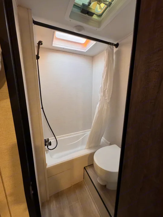 RV rental bathroom features a compact shower/tub combo, toilet, and ceiling vent for comfortable travel.. Grand River 25BH 2025